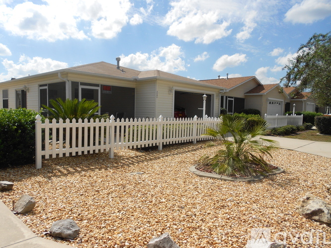 A white picket fence surrounds a house with a landscaped garden in front.