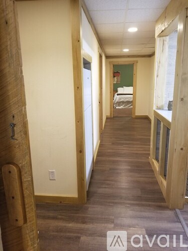 A hallway with wood floors and walls, leading to a bedroom.