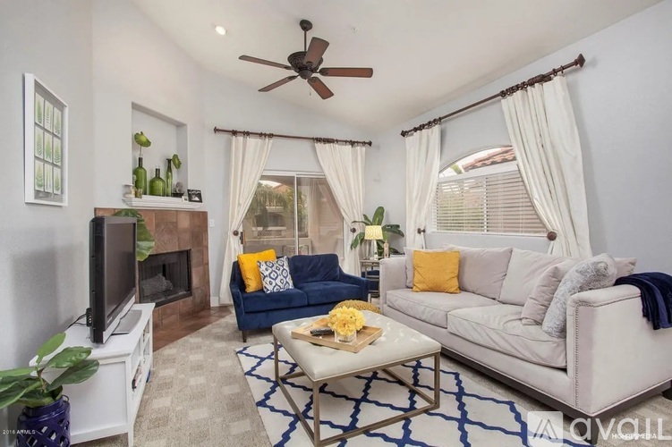 A living room with a white couch, a blue cushion, a television, and a ceiling fan.