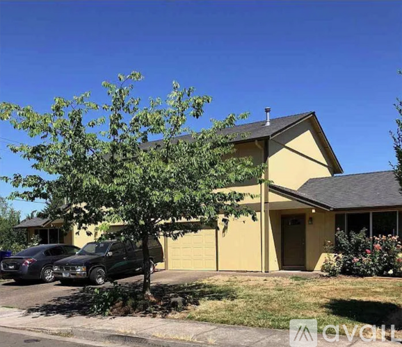 A yellow house with a tree in front and two cars parked in front.