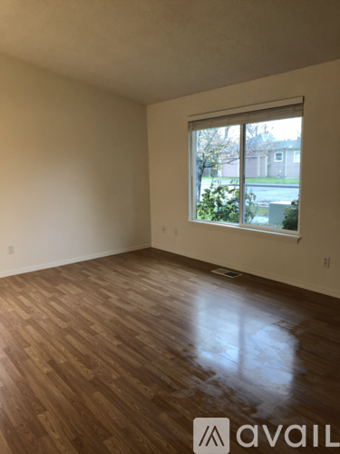 A room with wooden flooring and a window showing a view of a house.