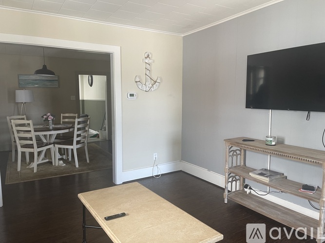 A living room with a television, a dining table and chairs, and a mirror.
