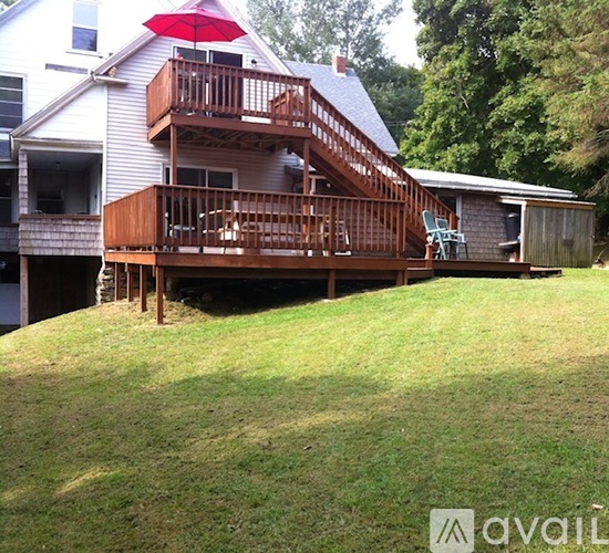 A wooden deck with a red umbrella is in front of a house.