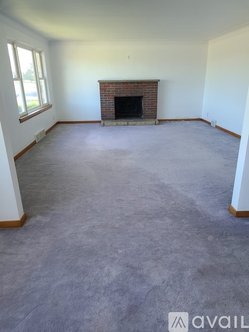 A large empty room with a fireplace and a window.