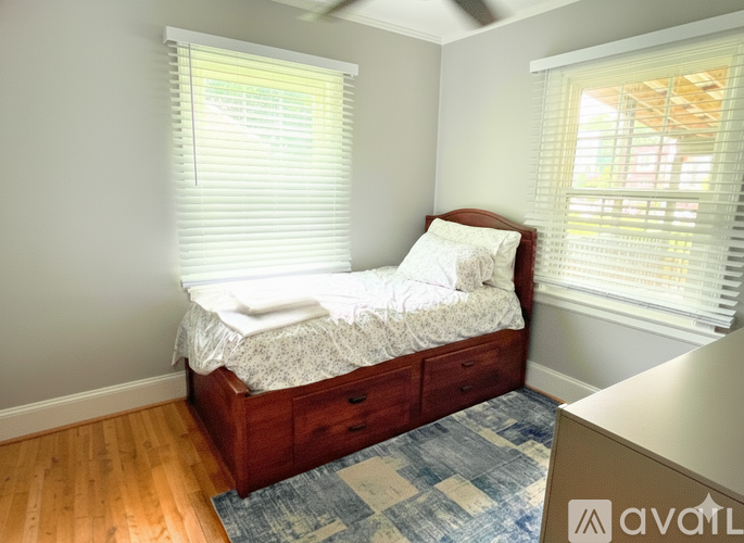 A bedroom with a bed, wooden drawers, and a window with blinds.