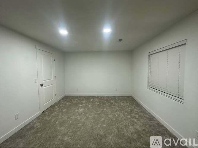 A room with a carpeted floor, a door, and a window with blinds.