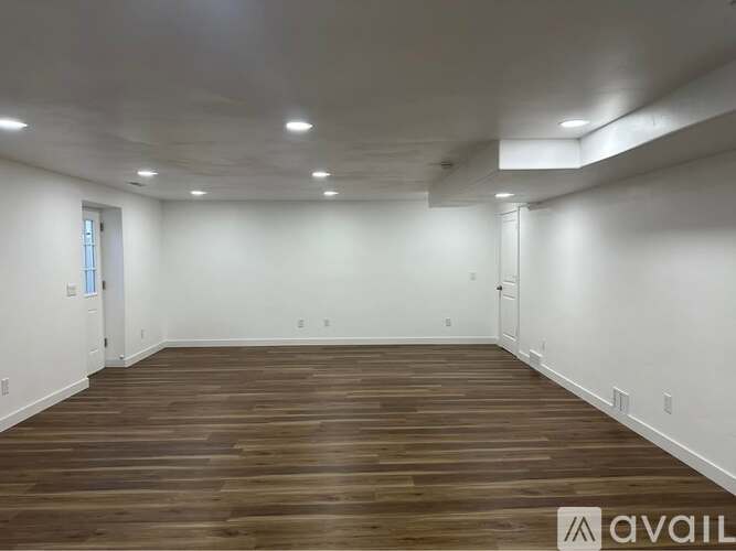 A spacious room with wooden flooring and white walls.