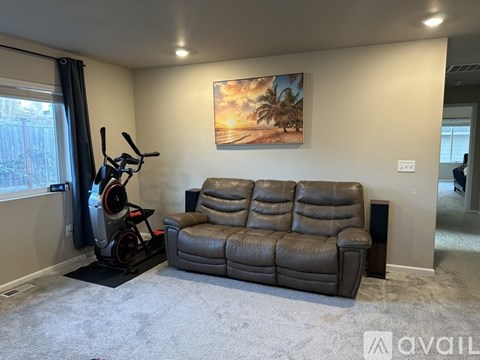A living room with a grey couch and a painting of a sunset on the wall.
