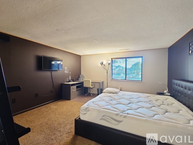 A bedroom with a large bed, a desk with a computer, and a window with blinds.