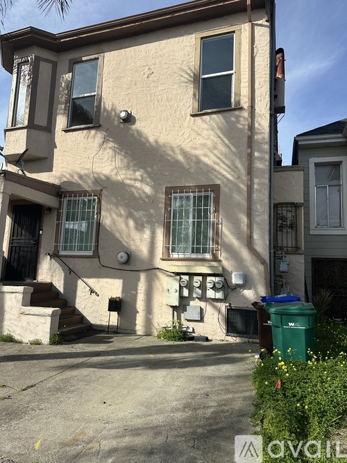 A beige house with a green trash can in front.