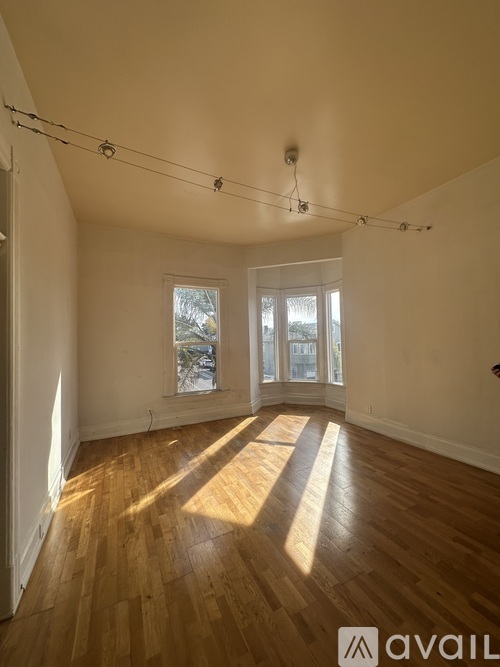 A room with wooden floors and white walls, with sunlight streaming in through the windows.