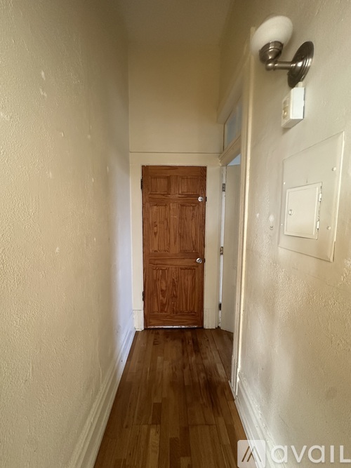 A hallway with a wooden door and a light on the wall.