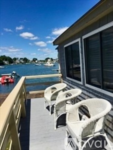 A row of white chairs are on a balcony overlooking a body of water.