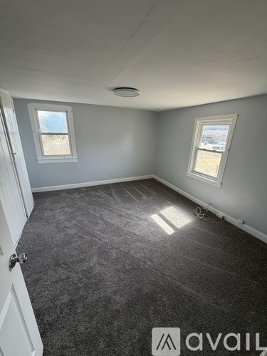 A room with grey carpet and two windows.