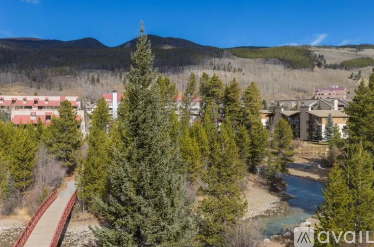 A river flows through a valley with a bridge crossing it and buildings in the background.