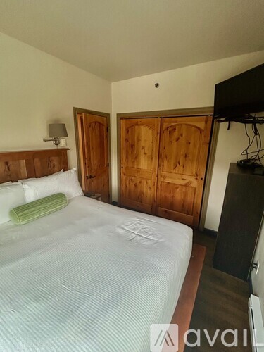 A bedroom with a bed, wooden wardrobe, and a television.