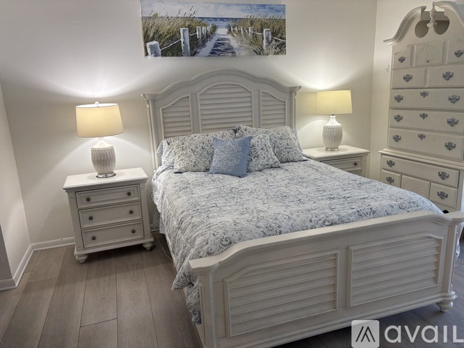 A bedroom with a large bed, two lamps, and a painting on the wall.