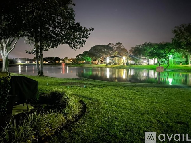 A nighttime scene of a park with a lake, trees, and a bench.