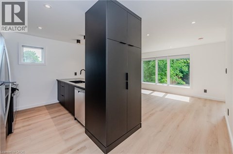 A black refrigerator in a kitchen with wooden flooring and a window.