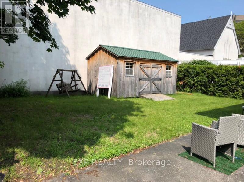 A small wooden shed with a green roof is situated in a grassy area.