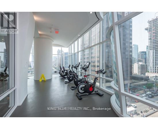 A gym with a row of stationary bikes and a view of the city outside the windows.