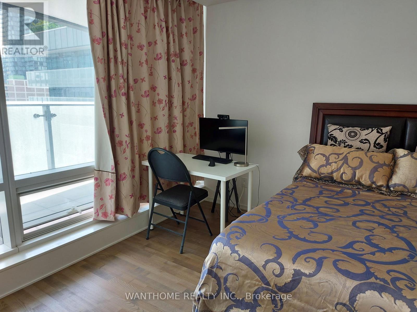 A bedroom with a bed, desk, chair, and window.