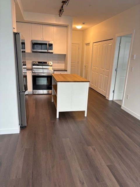 A kitchen with a refrigerator, microwave, oven, and cabinets.