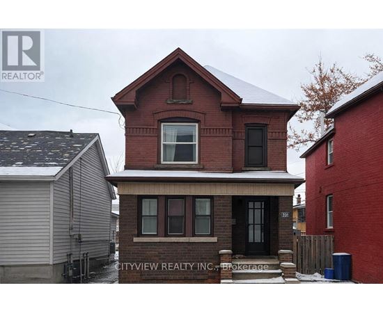 A red brick house with a black door and windows is in front of a grey house and a red building.