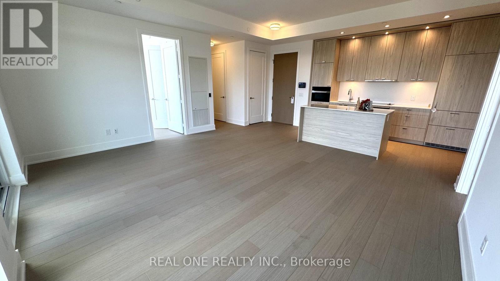 A spacious room with wooden flooring and a kitchen area with cabinets and a countertop.