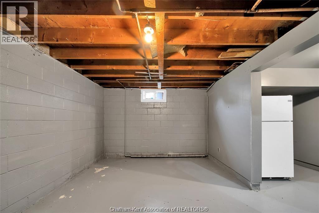 A spacious basement with a white refrigerator and exposed ceiling beams.