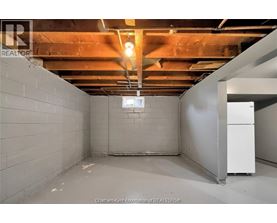 A spacious basement with a white refrigerator and exposed ceiling beams.
