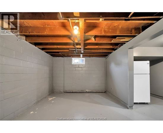 A spacious basement with a white refrigerator and exposed ceiling beams.