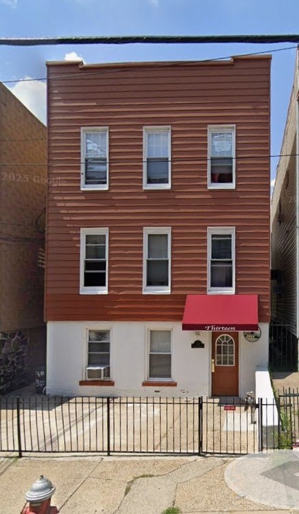 A brown building with a red awning is in front of a black fence.