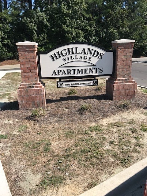 A sign for Highlands Village Apartments is displayed in front of a grassy area.