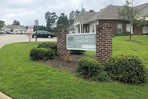 A sign for Maple Ridge Apartments is displayed in front of a brick pillar.