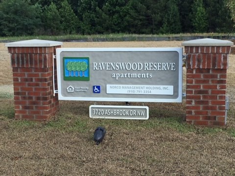 A sign for Ravenswood Reserve Apartments sits in front of a brick pillar.