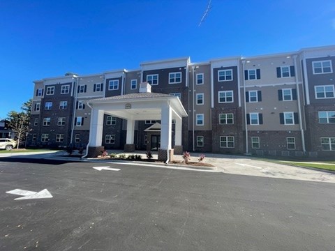 A large building with a white entrance and a parking lot in front.