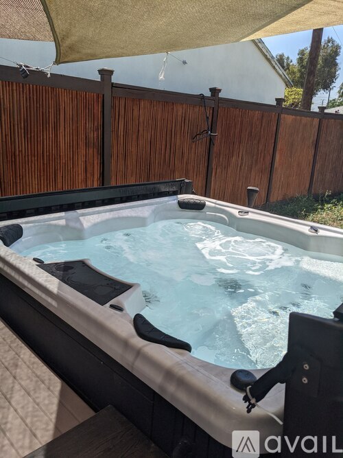 A hot tub with a control panel is surrounded by a wooden fence.