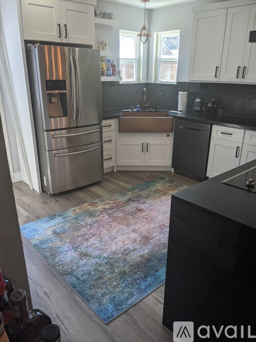 A kitchen with a refrigerator, cabinets, and a rug.