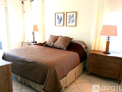 A bedroom with a large bed, two lamps, and two framed pictures on the wall.