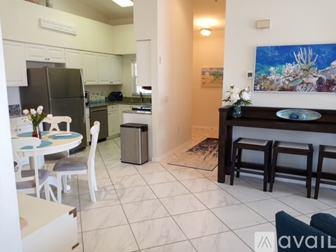 A kitchen with white chairs and a dining table with a vase of flowers on it.