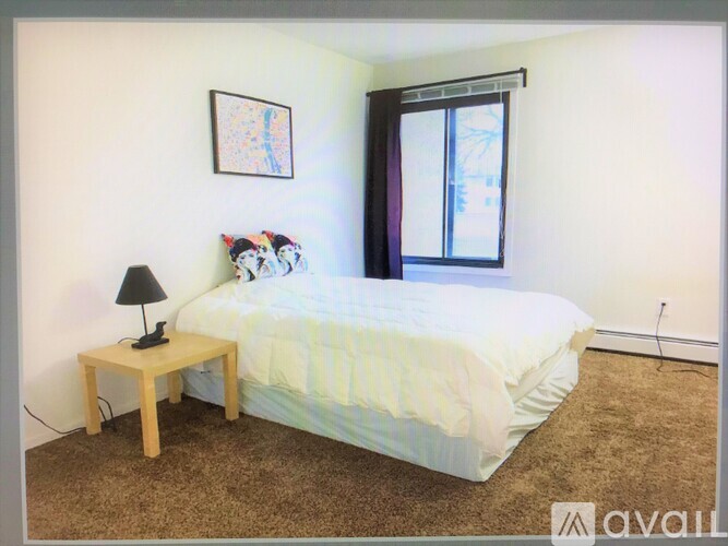 A bedroom with a bed, a nightstand with a lamp, and a picture on the wall.