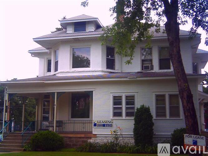 A white two story house with a porch and a tree in front.