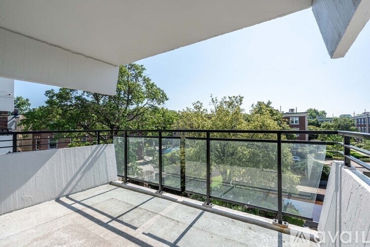 A balcony with a glass railing and a view of trees and buildings.