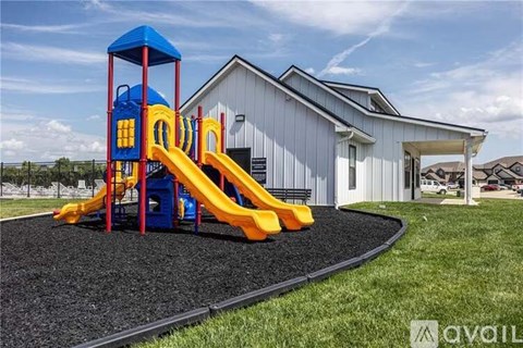 A playground with a yellow slide and a blue tower is in front of a white building.