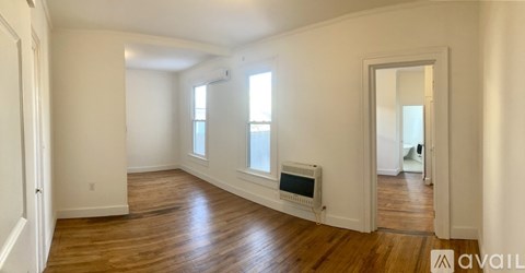 A spacious room with wooden floors and white walls, featuring a window and a door.