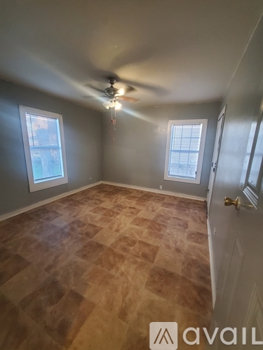 A room with a ceiling fan and light, two windows, and a wooden floor.