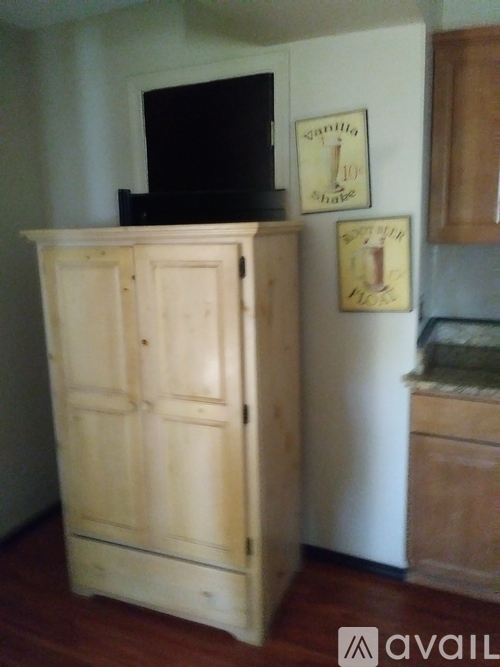 A wooden armoire stands in a kitchen next to a refrigerator.