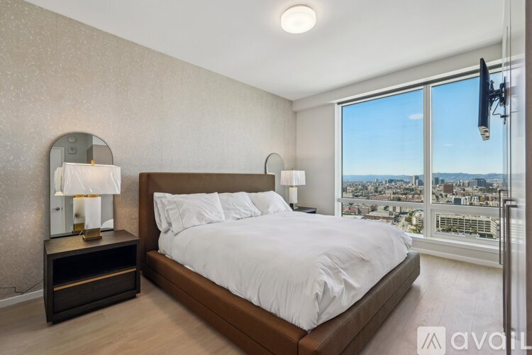 A bedroom with a large bed and a city view through the window.