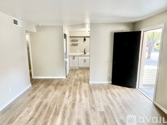 A spacious room with wooden flooring and a black door on the right.